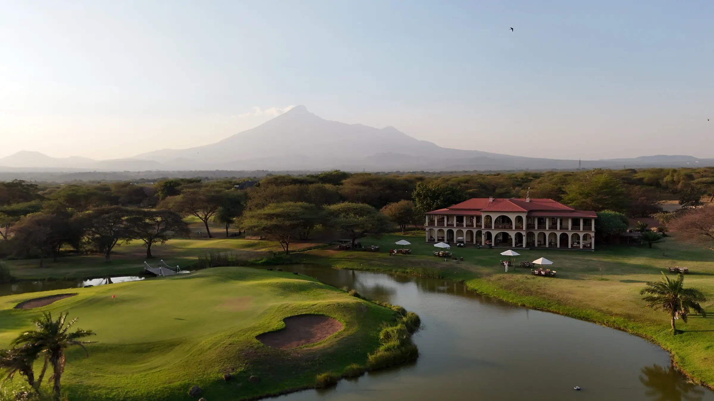 The KiliGolf clubhouse, green and lake in soft evening light, with a mountain beyond