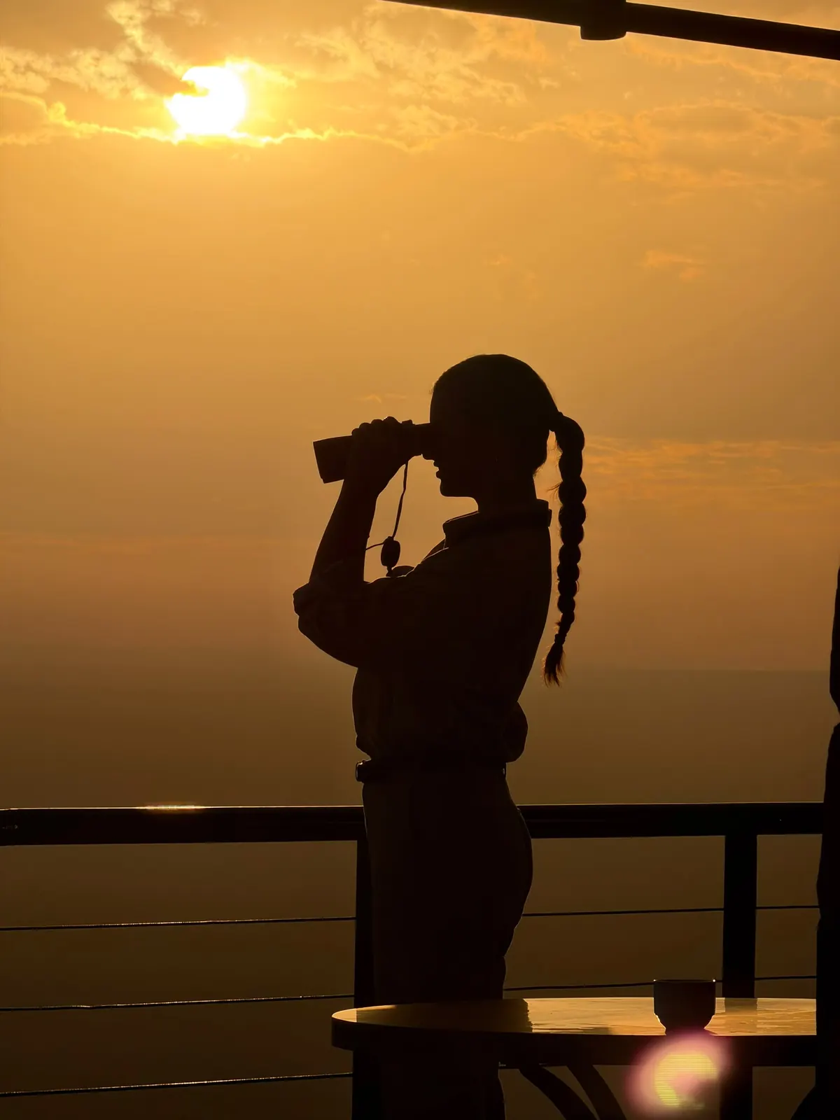 A traveller looking through binoculars at sunset over the plains